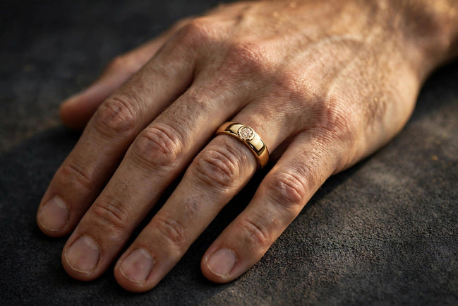Bezel-set solitaire diamond band in yellow gold, worn on a man's ring finger — MARWAH
