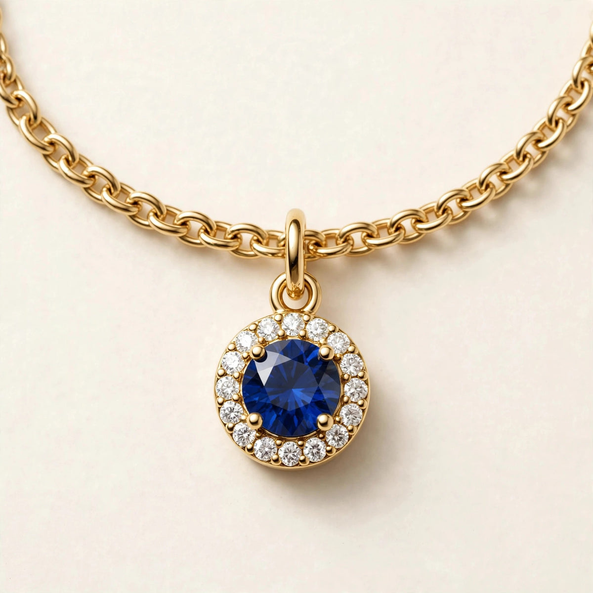 Birthstone Diamond Charm, blue sapphire with a diamond halo on a fine chain bracelet in yellow gold, charm detail view.