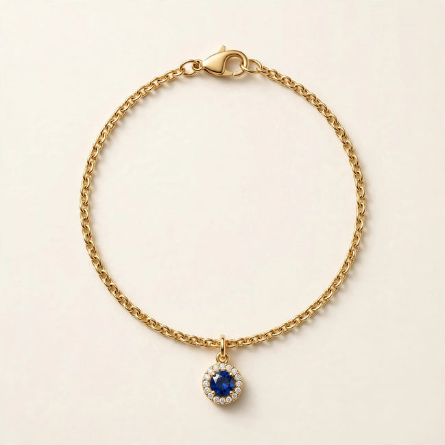 Birthstone Diamond Charm, blue sapphire with a diamond halo on a fine chain bracelet in yellow gold, full view.