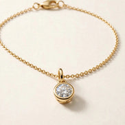 Solitaire Diamond Charm, round brilliant diamond in a slim bezel on a fine chain bracelet in yellow gold, charm detail view.