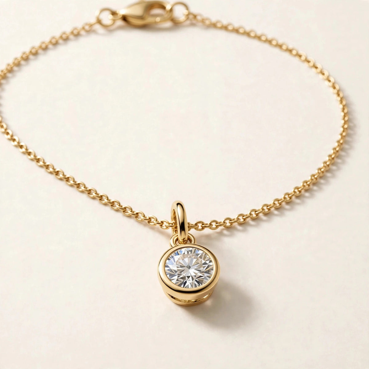 Solitaire Diamond Charm, round brilliant diamond in a slim bezel on a fine chain bracelet in yellow gold, charm detail view.
