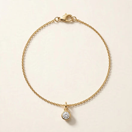 Solitaire Diamond Charm, round brilliant diamond in a slim bezel on a fine chain bracelet in yellow gold, full view.