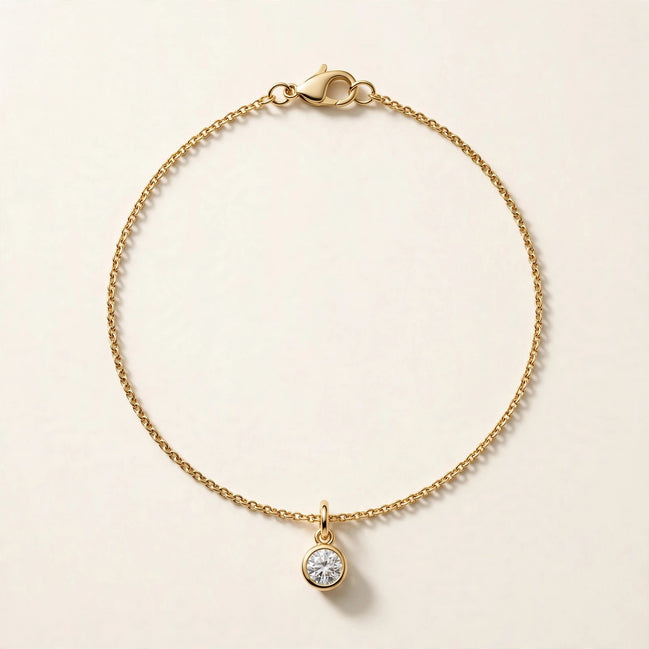 Solitaire Diamond Charm, round brilliant diamond in a slim bezel on a fine chain bracelet in yellow gold, full view.