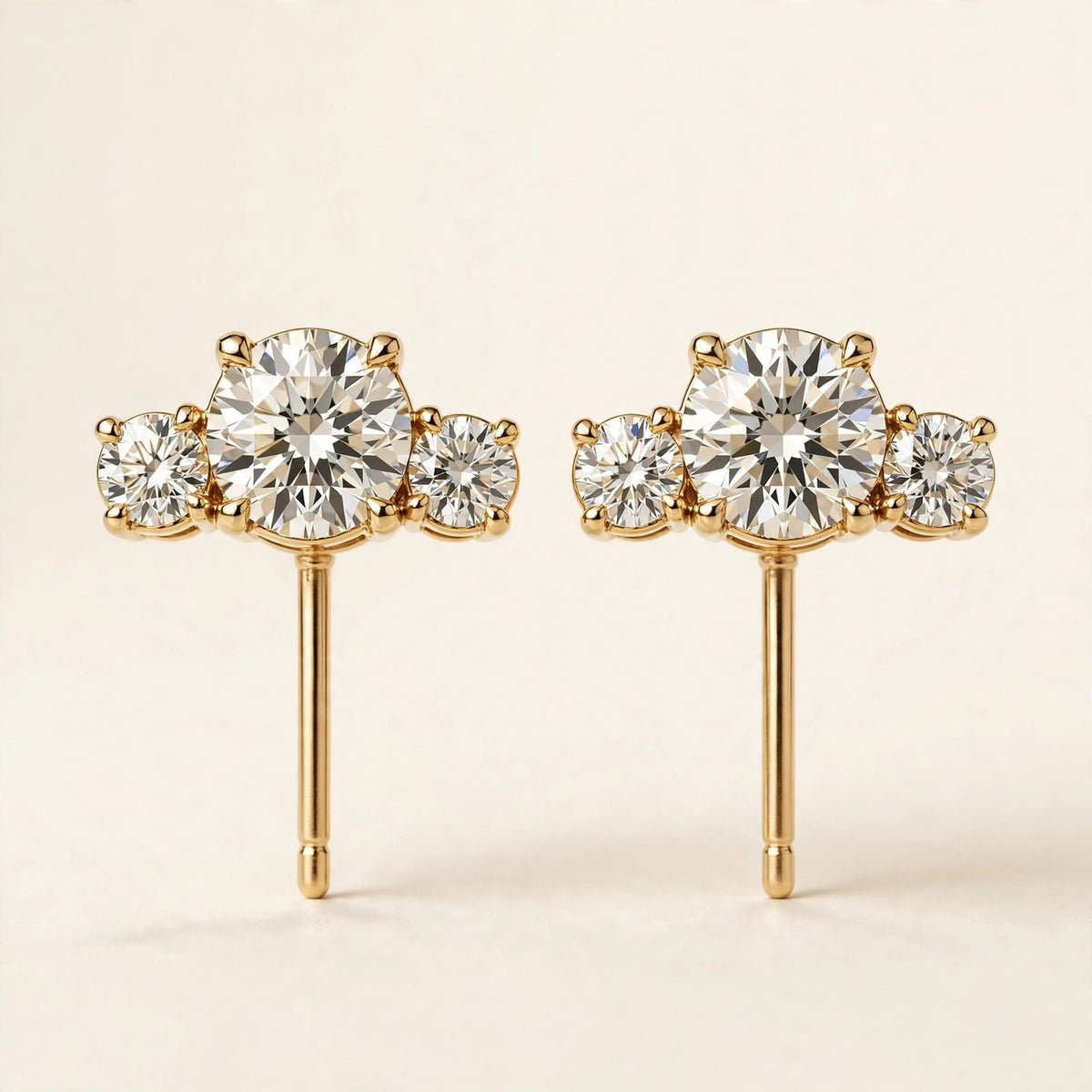 Three-Stone Diamond Studs, three graduated round diamonds in yellow gold, pair front view.