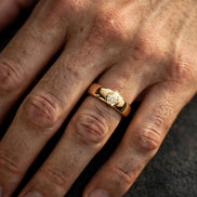 Bezel-set solitaire diamond band in yellow gold worn on a man's ring finger, alternate view — MARWAH