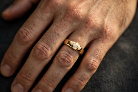 Bezel-set solitaire diamond band in yellow gold worn on a man's ring finger, alternate view — MARWAH