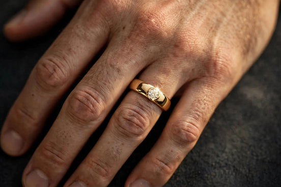 Bezel-set solitaire diamond band in yellow gold worn on a man's ring finger, alternate view — MARWAH